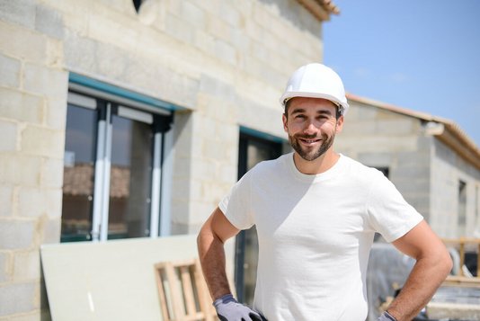 hausbau-haus-bauen-eigenleistung-rohbau-fenster-05 Freundlicher Handwerker vor einem Rohbau.